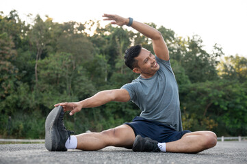 A happy, strong Asian man in sportswear is stretching his body on the floor outdoors