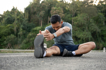 A happy, strong Asian man in sportswear is stretching his body on the floor outdoors