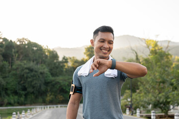 A happy, fit Asian man is checking his calories burning on his smartwatch after running in a park.