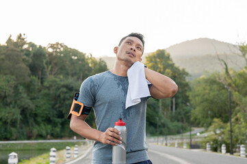 Fototapeta premium A tired Asian man is wiping his sweat on his face, resting after a long run outdoors in the morning.
