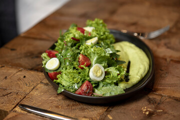 Person eating Fresh green salad with quail eggs, cherry tomatoes and guacamole in black plate on grey background