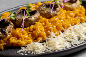 Pumpkin risotto with mushrooms and parmesan cheese on black plate