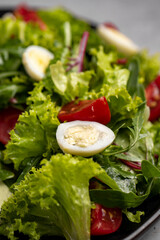 Fresh green salad with quail eggs, cherry tomatoes and guacamole in black plate on grey background