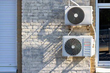 Two external air conditioners installed outside on an old brick wall near new metal-plastic windows.