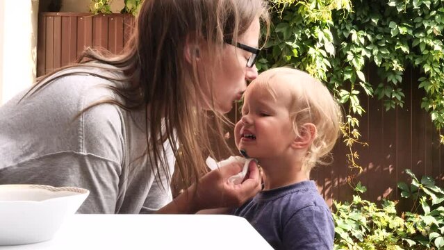 The mother is tending to a small cut on her son's chin. She applies antiseptic to wound, which causes child some discomfort.The mother then kisses her very distressed two-year-old son on forehead.