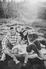 Mother, father, daughter, son sitting on blanket, hugging in grass in field at sunset. Children embrace parents. Happy young family walking spending time together in nature. Black and white photo