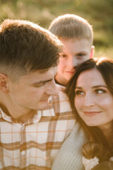 The son hugging parents on nature. Mom, dad embrace child walking in grass. Happy young family with kids spending time together, outside, on vacation, outdoors. Concept of family holiday.