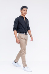 Fototapeta premium Handsome and fashionably cool asian guy taking a stroll, wearing black polo shirt and khaki pants. Moving to the right. Full body photo, isolated on a white background.