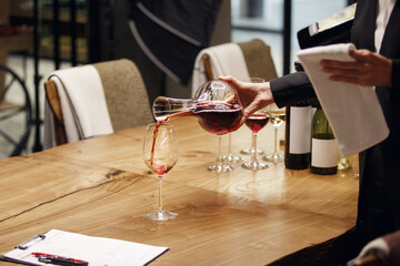 Professional female sommelier pours red wine from decanter to the glass, close up image. Woman...