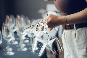 Woman waiter takes few empty wine glasses from bar table, close up without face. Restaurant service...