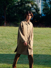 Portrait of a handsome Chinese young man with curly hair in khaki overcoat walking on green grass...