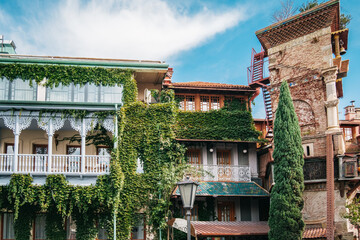 Beautiful traditional georgian house with vines climbing the wooden balcony next to the Leaning Clock Tower in Tbilisi Old town, Georgia