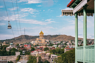 View of the Sameba Cathedral, the Tbilisi ropeway, and a traditional Georgian wooden balcony in...