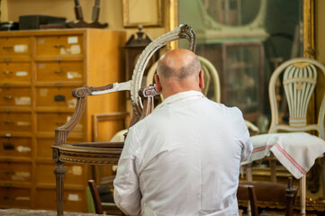Artigianato, artigiano. Restauro di sedia d'antiquariato, artigiano restauratore stende il gesso ...