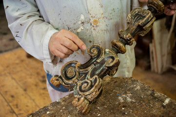 Artigiano restauro, mostra in primo piano candelabro da restaurare. Dorato, doratura, d'antiquariato.