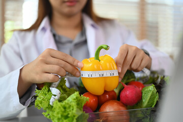 Close up dietitian holding measuring tape around fresh bell pepper. Dieting, health food and weigh...