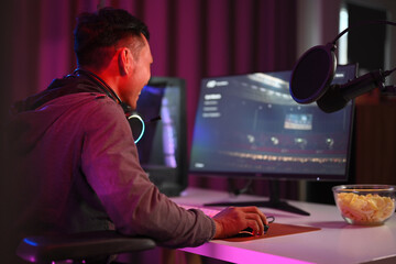 Side view shot man streamer playing online video game on personal computer in neon room.