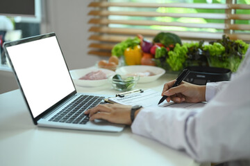 Closeup view professional nutritionist using laptop and prescribing recipe at working desk. - obrazy, fototapety, plakaty