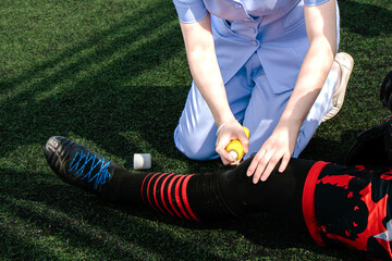 nurse is helping football player who has a leg injury while playing football in the grass.
