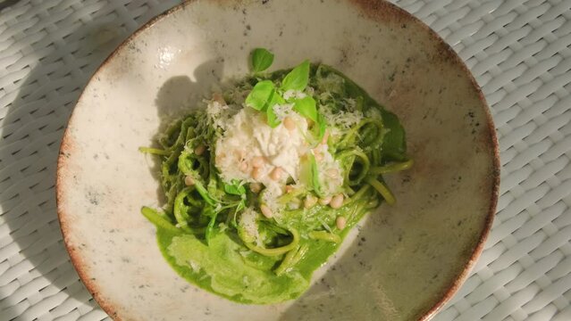 Serving pasta with pesto and stracciatella cheese in restaurant. Italian cuisine dish.