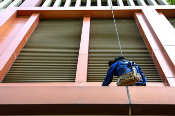 Back view high rise cleaner worker with rope access cleaning fa cade windows, risk and dangerous...