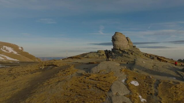 aerial orbti shot of a man hiker standing on top of rock next to romanian bucegi sphinx in mountains during sunset