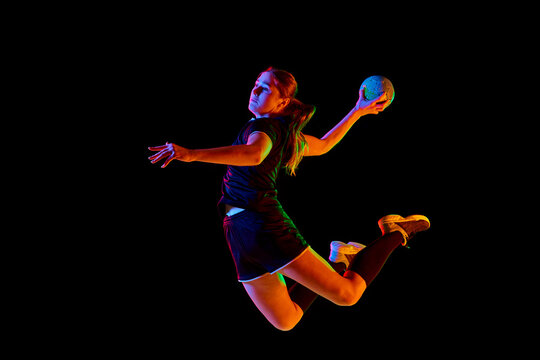 Fit, young, competitive female handball player demonstrating throwing techniques against black background in neon light. Concept of professional sport, movement, dynamic, workout, championship 2024