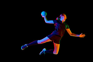 Fototapeta na wymiar Fit, focused woman engaged in handball drills, displaying determination and focus against black background in mixed neon light. Concept of sport, hobby, movement, dynamic, championship, goal. Ad