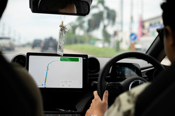 Back seat view of traveler man driver driving an EV car and using GPS navigation map on tablet touch screen during road trip. - obrazy, fototapety, plakaty