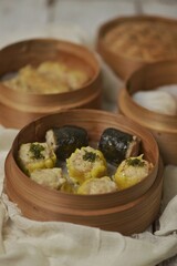 Various type of dim sum in bamboo streamer, such as har gow or hakau, shumai or siomay, tofu skin roll, spring roll and fried noodle shumai. Served with chili oil sauce.