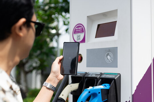 Electric car charging at the station. Sustainability and renewable energy concept. Electric vehicle (EV) fuel advance, save the earth conception. QR code payment with mobile phone