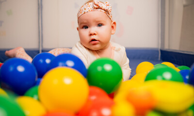 Obraz premium Cute baby girl playing with colorful balls in kindergarten.