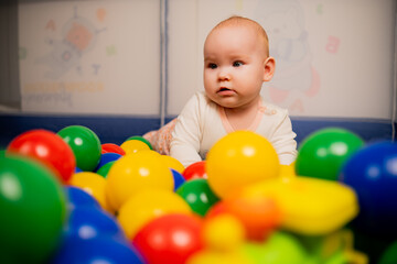 Fototapeta na wymiar Cute baby girl playing with colorful balls in kindergarten.