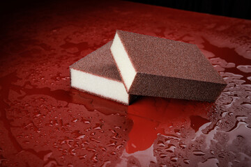 Melamine sponge on red wet background. Beautiful drops of water around a melamine sponge.
