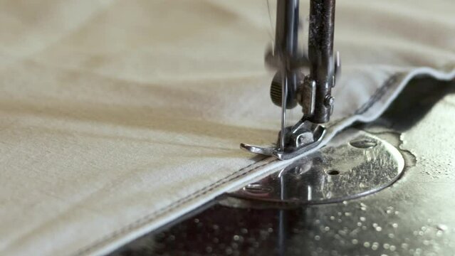 Sewing Machine Needle in Motion. Close-up of sewing machine needle rapidly moves up and down. The tailor sews fabric on the sewing workshop. The process of sewing fabric.