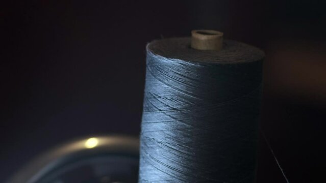 Process of sewing fabric. Closeup skein of black thread on a working retro sewing machine. Blurred background. Unwind the thread. skeins of thread. Concept of tailoring, women's hobby.