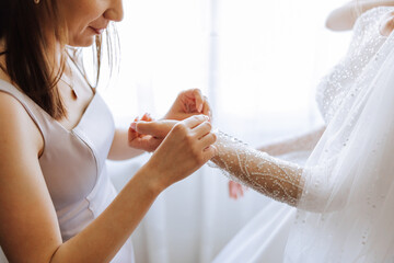 Morning of the bride. The bride's maid of honor helps the bride lace up her dress, fasten buttons...