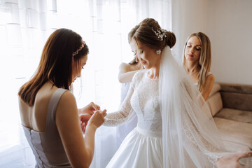 Morning of the bride. The bride's maid of honor helps the bride lace up her dress, fasten buttons...
