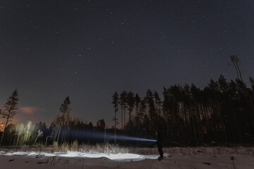 Night scene, a man with a flashlight in the winter forest. Starry sky. - obrazy, fototapety, plakaty
