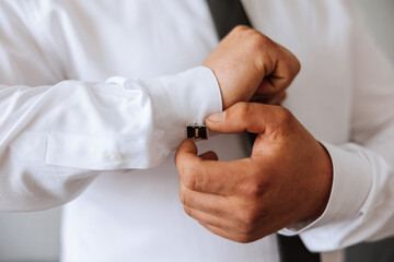 handsome business man buttoning shirt sleeves at home. The groom is preparing for the wedding. Close-up photo.