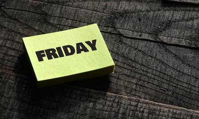 FRIDAY word on a small piece of paper and wooden table.