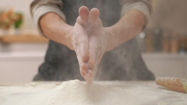 A cook in the kitchen sifts flour through a sieve. Kneading raw dough with male hands. Breaks an egg. White flour.