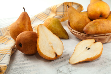 Whole and halves of pears, wicker basket and yellow kitchen towel on white wooden background..