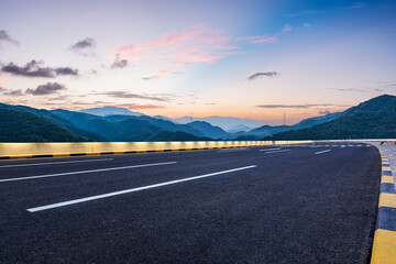 Asphalt highway road and green mountains with sky clouds at dusk