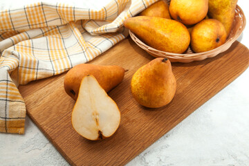 Cutting board with whole and halves pears, wicker basket and yellow kitchen towel on white wooden background..