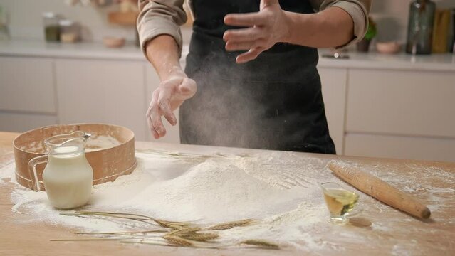 A cook in the kitchen sifts flour through a sieve. Kneading raw dough with male hands. Breaks an egg. White flour.