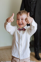 happy little boy in a white shirt, in the room, joyfully shows a thumbs up. Joyful child. Sincere emotions.