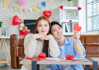 Asian young handsome male boyfriend sitting on sofa smiling cuddling with beautiful female...