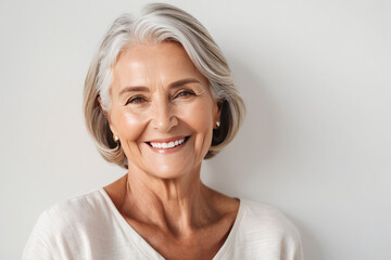 Portrait of beautiful older woman smiling and standing by white wall. A place for text, a banner for advertising. - Powered by Adobe