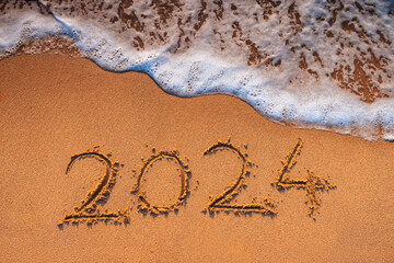 Happy New Year 2024 text written on the beach sand and caribbean blue sea waves, travel and lifestyle concept